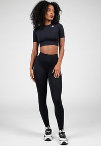Black short-sleeved crop top with textured accents, paired with high-waisted black leggings. Both garments are form-fitting and stretchy.