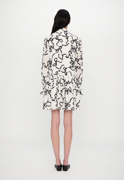 Rochie albă cu un model abstract de fundă neagră, mâneci lungi, tiv ondulat și croială slim. Materialul neted și designul stratificat adaugă textură.