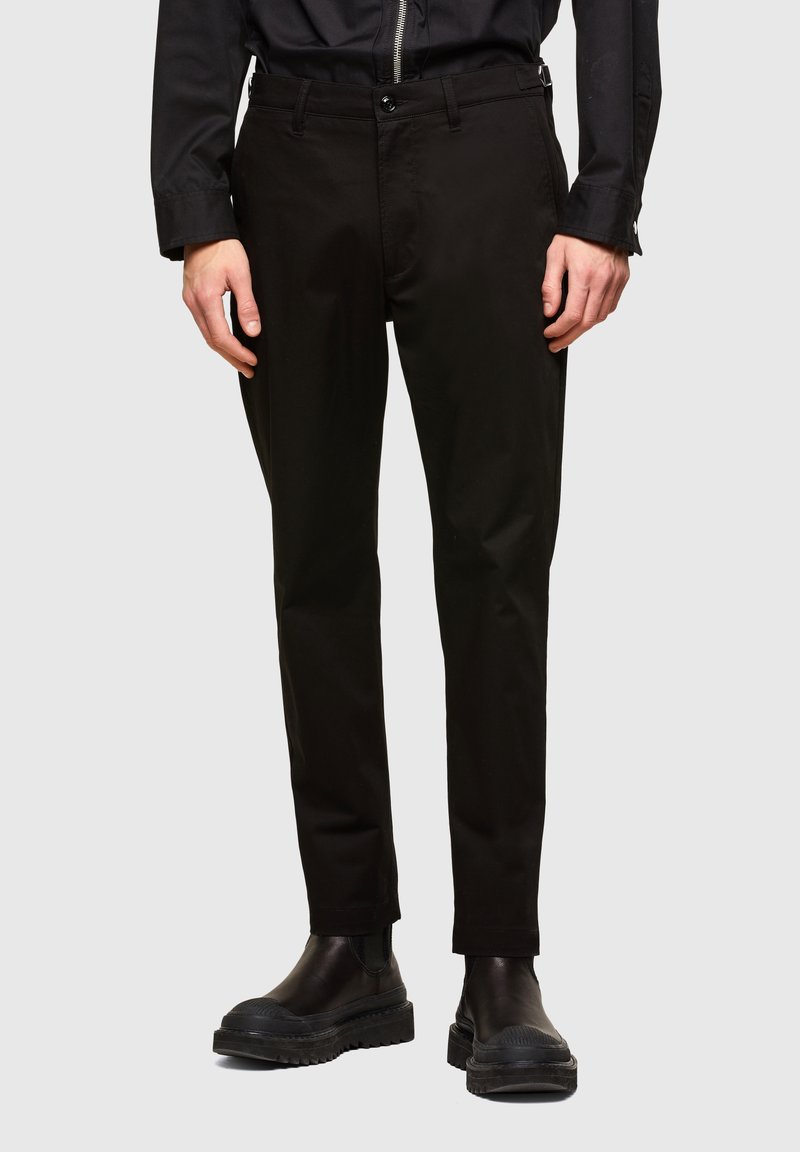 Černé kalhoty se rovnými nohavicemi, vyrobené z odolné látky. Mají zapínání na knoflík, boční kapsy a slim fit střih. Nosené s černými botami.