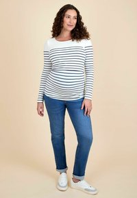 Langærmet graviditetsbluse i hvid med marineblå vandrette striber; parret med lyseblå jeans og hvide sneakers. Blødt stof, tætsiddende pasform.