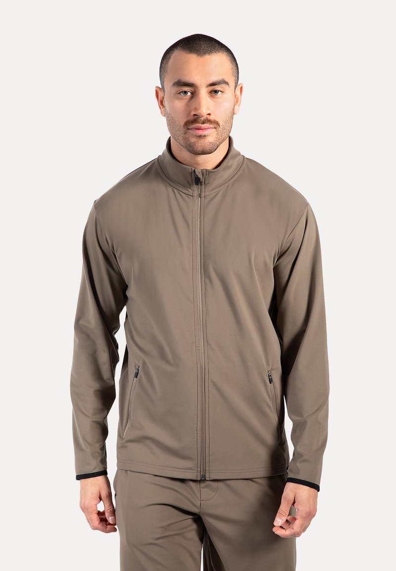 Herren Zip-Jacke in Hellbraun, aus einem glatten Stoff gefertigt. Verfügt über zwei Seitentaschen und einen hohen Kragen.