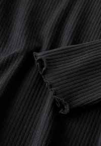 Schwarzer gerippter Stoff mit einer strukturierten Oberfläche. Das Material weist am Rand des Ärmels ein geschlungenes Saumdetail auf.