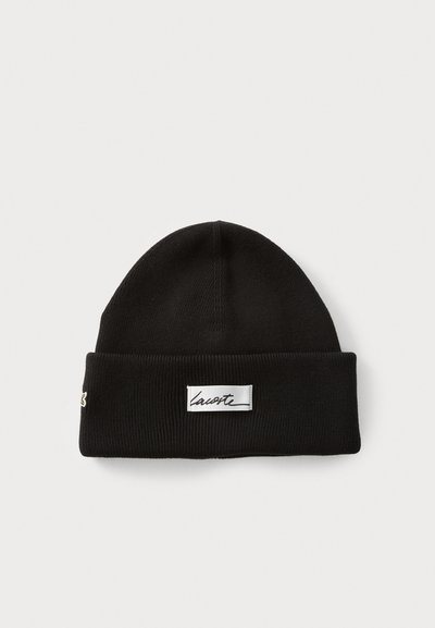 Bonnet en tricot noir avec un revers, présentant une pièce rectangulaire blanche avec un texte en cursive et un petit logo brodé sur le côté.