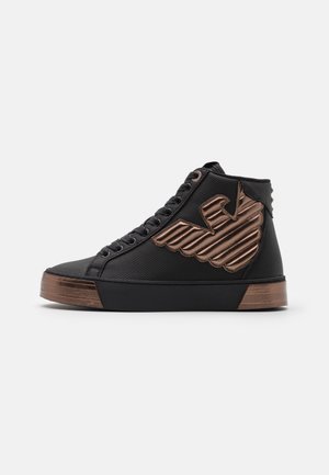 Baskets montantes noires avec lacets noirs et grand logo ailé métallique cuivre sur le côté, accents cuivrés sur la semelle.