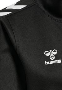 Zwarte sporttop gemaakt van gladde stof, met een hoge halslijn, wit logo en een kenmerkend wit chevronpatroon op de schouder.