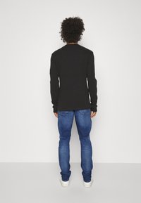 Czarna koszula z długim rękawem i okrągłym dekoltem, połączona z niebieskimi dżinsami i białymi trampkami. Prosty fason z prążkowanymi mankietami i dołem.