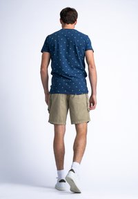 T-shirt marine avec motif de pois verts, associé à un short cargo en kaki. Le modèle porte des baskets blanches avec des accents verts et des chaussettes blanches.