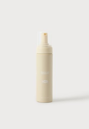 Botella de spray beige de limpiador y acondicionador UGG con tapa de plástico transparente sobre fondo blanco.
