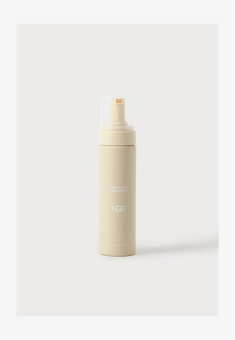 Flacon spray beige de nettoyant et soin UGG avec un bouchon en plastique transparent sur fond blanc.