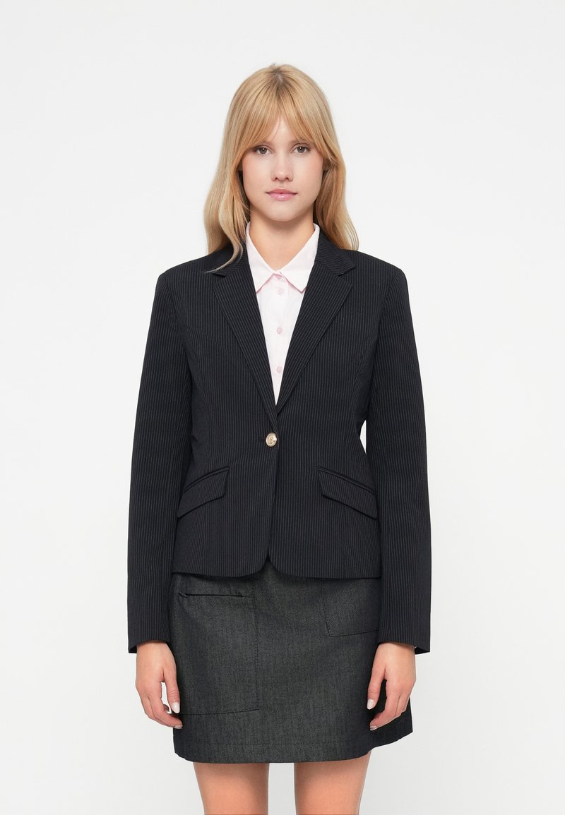 Blazer noir à rayures avec revers notés et deux poches avant, associé à une jupe grise au fini texturé et avec poches avant.