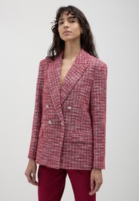 Blazer doppiopetto in tessuto tweed rosa, caratterizzato da un motivo testurizzato, rever a lancia e bottoni in tono oro. Vestibilità sartoriale con tasche laterali.