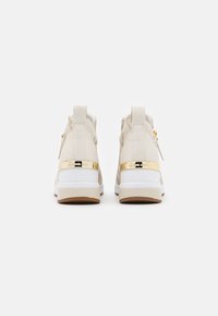 Sneaker alte beige con accenti dorati, pannelli testurizzati, una suola intermedia bianca e una suola in gomma. La parte posteriore presenta un'etichetta per il pull e dettagli con zip.
