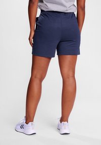 Marineblå sportshorts med elastisk midja, slät textur och sidfickor, kombinerat med vita sneakers med grå detaljer.