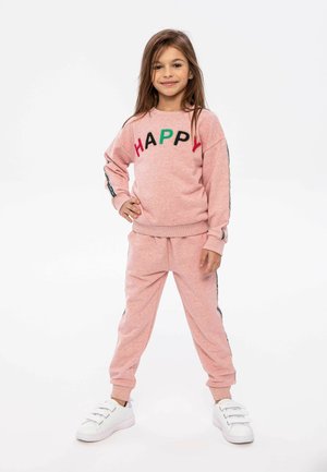 Roze sweatshirt met "HAPPY" geborduurd in kleurrijke letters, gecombineerd met bijpassende sweatpants. Witte sneakers met drie banden.