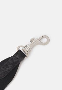 Mousqueton pivotant argenté fixé à l'extrémité d'une sangle en cuir noir texturé sur fond blanc.