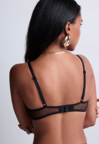 Soutien-gorge noir avec des détails en maille transparente, des bretelles réglables et une fermeture à crochets au dos. Présente un design minimaliste et une texture lisse.