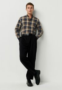 Checkered button-up shirt in beige and blue, black wide trousers, black lace-up shoes, and a black belt. Smooth textiles, structured fit.