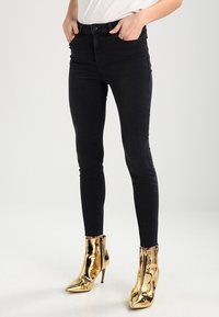 Černé skinny džíny s vysokým pasem vyrobené z denimu, s knoflíkovým zapínáním a předními kapsami, spárované s metalickými zlatými kotníkovými botami.