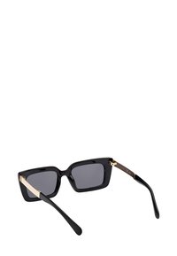 Sorte firkantede solbriller med mørke linser og guldmetal accenter på stængerne, set bagfra på en hvid baggrund.