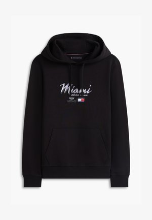 Fekete kapucnis pulóver első zsebbel, "Miami 2026 május 1-3" felirattal, Cadillac logóval és Tommy Hilfiger zászlóemblémával a mellrészen.