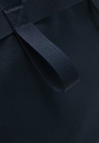 Gros plan d'une poignée en boucle en tissu noir cousue sur une surface textile sombre, montrant la texture et les coutures renforcées.