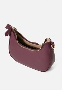 Geantă din piele sintetică burgundy cu închidere cu fermoar, accesorii în nuanță de aur și un mic fundiță pe o latură. Textură netedă și formă curbată.