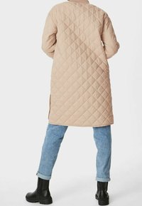 Beige vadderad lång kappa med rak siluett, sidokil och rundad halsringning, matchad med ljusblå jeans med uppvikta ärmar och svarta ankelskor.