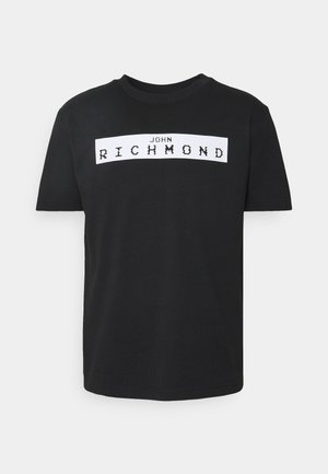 Schwarzes T-Shirt mit kurzen Ärmeln und Rundhalsausschnitt, auf der Brust ein weißes rechteckiges Druckfeld mit dem Schriftzug "JOHN RICHMOND" in stilisierten Blockbuchstaben.