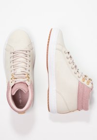 Zapatillas altas beige con acentos de punto rosa texturizado, ojales dorados y suela de goma blanca. Material de ante suave con detalles de costura.