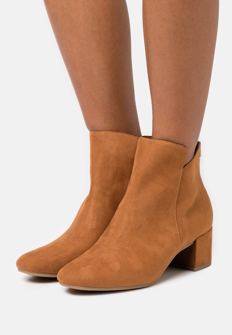 Mujer llevando botines de ante color beige hasta la mitad de la pantorrilla, con tacones bajos en bloque, textura suave y puntas redondeadas, sobre un fondo blanco.