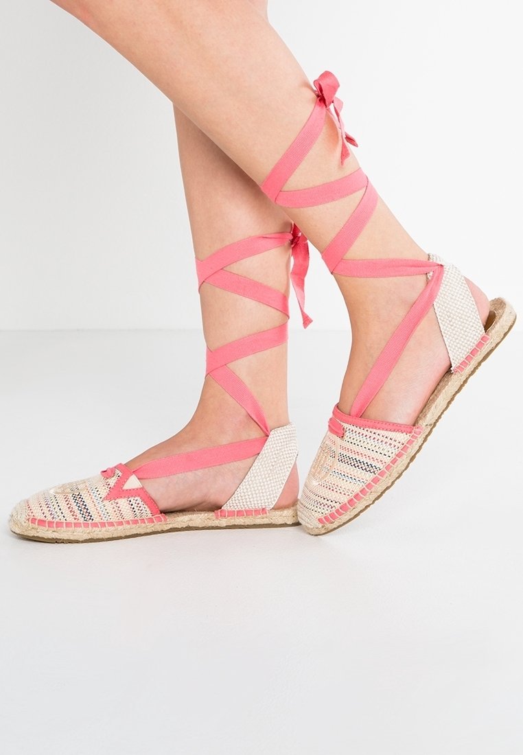 Alpargatas planas con un upper de fibra natural tejida y lazadas de cinta rosa. La suela está hecha de yute, proporcionando un acabado texturizado.