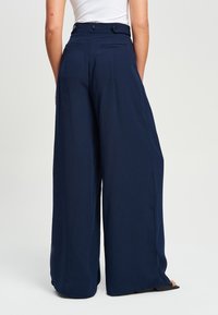 Mornarske široke hlače s visokim strukom, glatkog materijala, s dva stražnja džepa i dugmetom za zatvaranje na leđima.