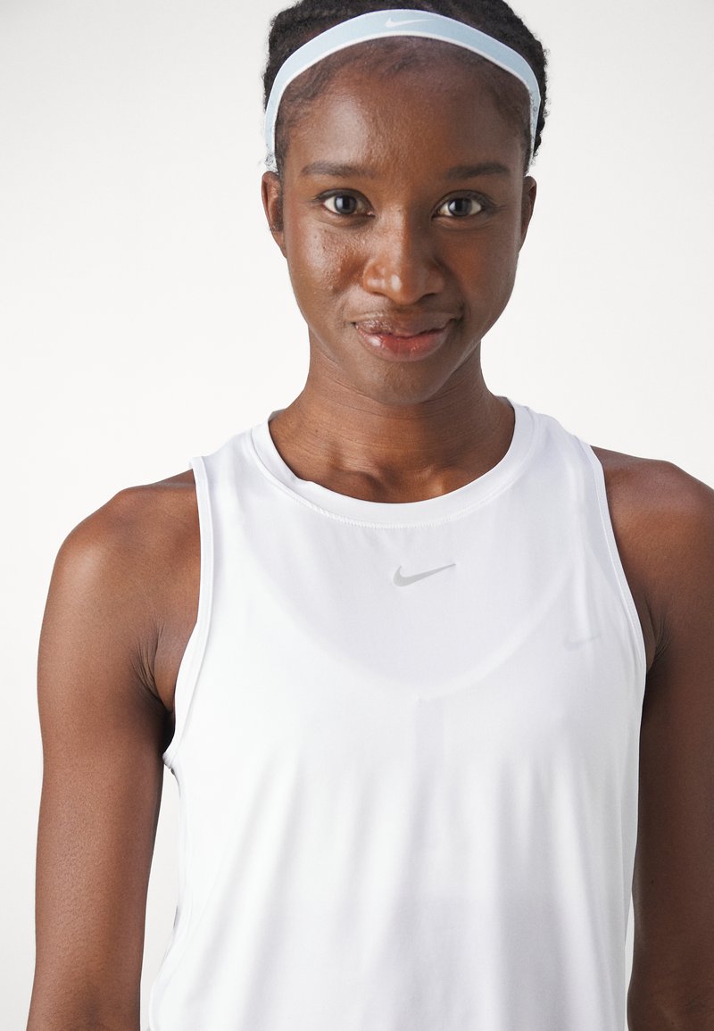 Top atlético sin mangas de color blanco con un escote redondo, que presenta un pequeño logotipo gris de Nike en el pecho y una cinta para la cabeza azul claro. Textura suave.
