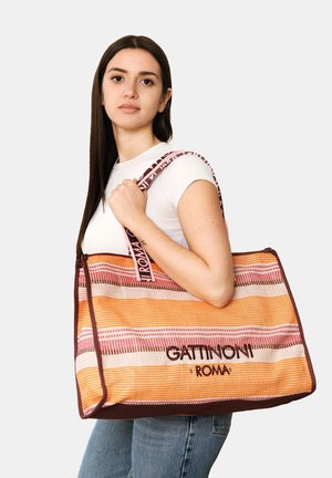 Jonge vrouw draagt een grote gestreepte draagt tas met het logo "Gattinoni Roma" op de schouderband en de tas.