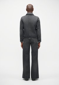 Donkergrijze denimjacket met bijpassende wijde jeans. Kenmerken zijn onder andere een kraag, voorzakken en een licht getailleerde snit bij de taille.