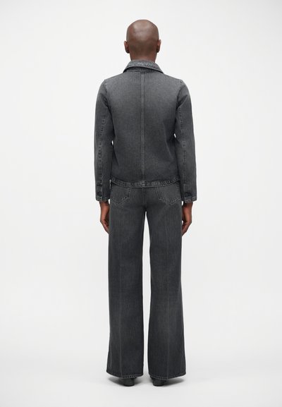 Tumši pelēki džinsu jaka ar atbilstošām platām biksēm. Iespējas ietver apkakli, priekšējās kabatas un nedaudz pieguļošu siluetu viduklī.