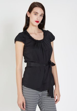 Blusa negra de manga corta con escote volado y cintura fruncida, combinada con pantalones estampados con un diseño de rombos.