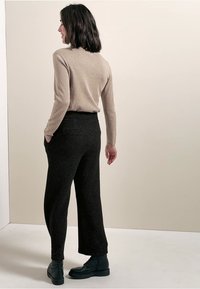 Beige aansluitende trui met lange mouwen, gecombineerd met zwarte broek met wijde pijpen en een gestructureerd patroon, afgemaakt met zwarte veterschoenen.