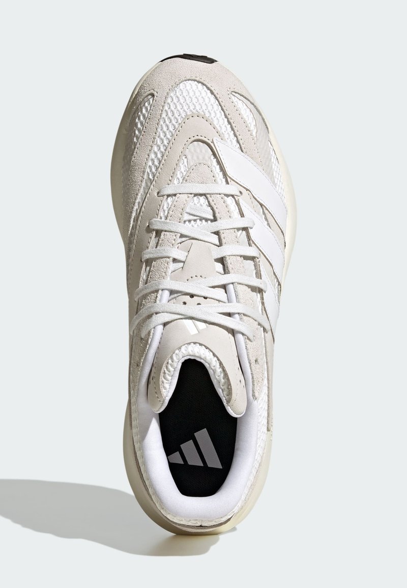 Helle beigefarbene Sportschuhe mit Obermaterial aus Mesh und Wildleder, featuring weiße Streifen, runde Zehenpartie und einem schwarzen Innenraum mit einem Logo.