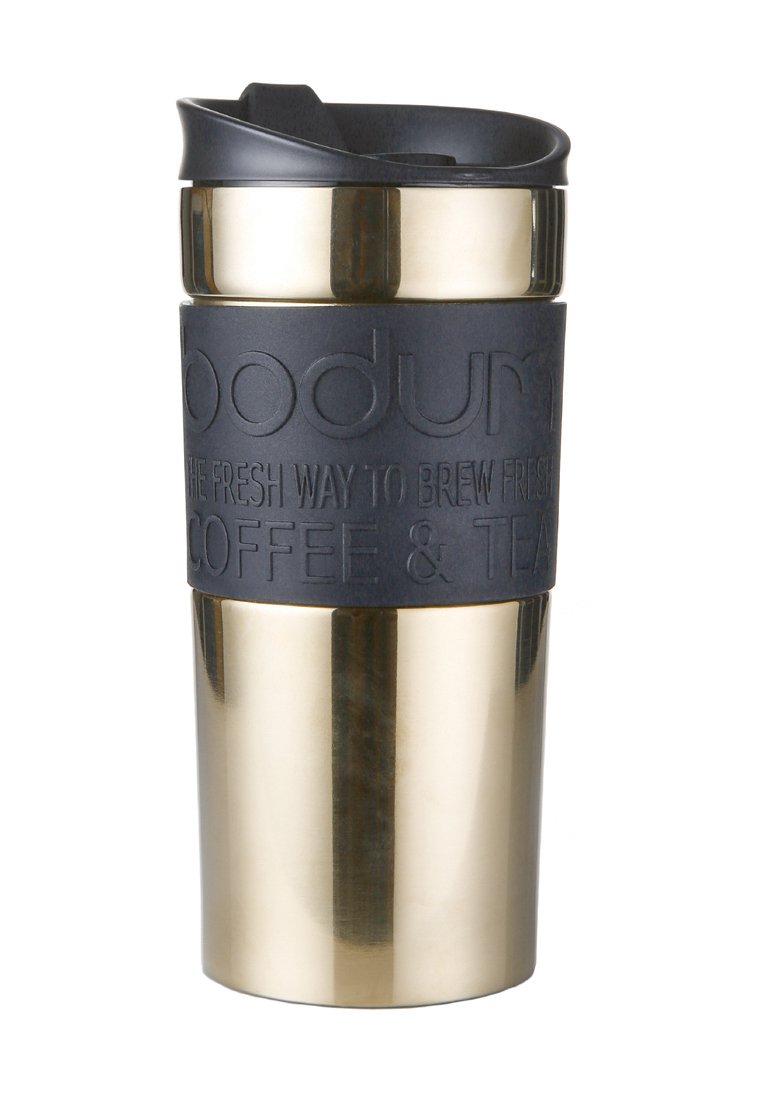 Taza de viaje de acero inoxidable dorado con un agarre de silicona negra mate, que presenta texto en relieve, una tapa atornillable y una forma cónica para facilitar su sujeción.