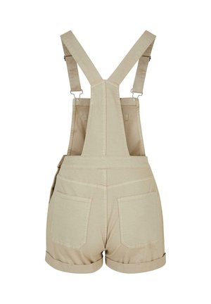 Bež bombažni kratki kombinezon s nastavljivimi naramnicami, dvema zadnjima žepoma in zavihano spodnjim robom, prikazan od zadaj na belem ozadju.