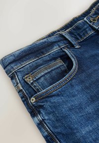 Jeanși din denim albastru închis cu un design clasic, având o buzunar frontal și accente de cusătură vizibile. Textură moale și zone ușor decolorate.