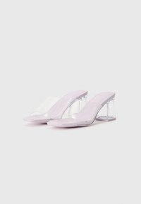 Mules dengan tumit bening yang menampilkan bodi berwarna lavender, tali transparan, dan tumit geometri yang chunky. Tekstur halus dengan desain minimalis.