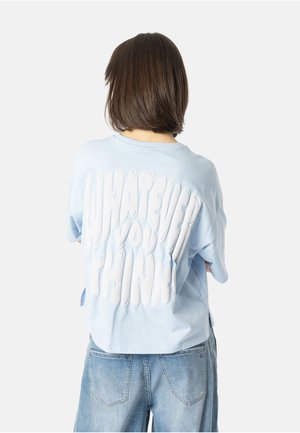 Lyseblå oversized t-shirt med et hvidt tekstureret grafik på ryggen, der har sætningen "WHAT EVER YOU THINK!" i en rund skrifttype.