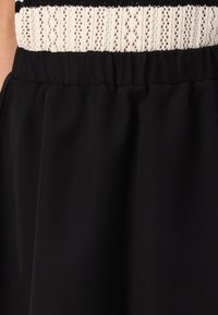 Ceinture noire d'une jupe avec du tissu froncé ; le haut présente une texture tricotée, à motif blanc et noir. Matière lisse et douce.