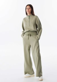 Lichtgroen ritsvest met hoge kraag, gecombineerd met bijpassende wijde broek. Zachte textuur, casual pasvorm en broek met trekkoord.