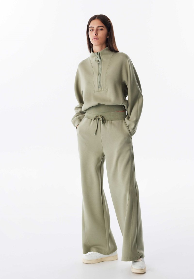 Lichtgroen ritsvest met hoge kraag, gecombineerd met bijpassende wijde broek. Zachte textuur, casual pasvorm en broek met trekkoord.