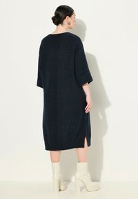 Abito lavorato a maglia blu navy con maniche corte e fessure laterali, caratterizzato da una vestibilità comoda e dettagli a coste. Abbinato a stivali bianchi con tacco largo.