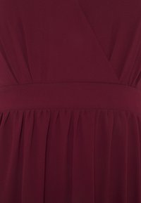 Robe bourgogne en tissu léger plissé avec une texture lisse, taille cintrée et design enveloppant.