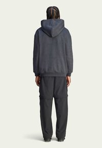 Musta huppari, jossa on teksturoitu kuvio, yhdistettynä löysiin mustiin housuihin. Rentoon tyyliin kuuluva malli, joka on mukava päällä.